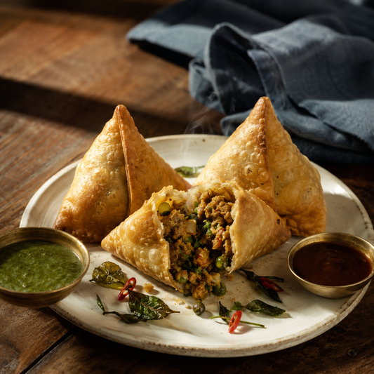 Chicken Samosa — three crisp golden samosas with one broken open showing minced chicken and pea filling, alongside mint and tamarind chutney bowls